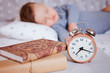© tumskaia - the alarm clock stands on a shelf with books, in the background the baby sleeps in a baby bed