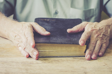 Wall Mural - A man is praying to God upon holy bible on wooden table with window light bokeh, vintage color.