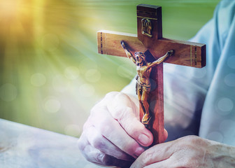 Wall Mural - A man hands holding the crucifix on wooden table with window light and bokeh effected. christian background and copy space.