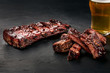 Pork ribs in barbecue sauce and a glass of beer on a black slate dish. A great snack to beer on a dark stone background. Top view with copy space