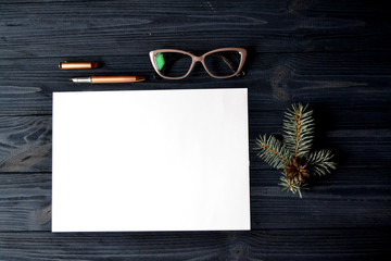 Wall Mural - The sheet of white paper with pen, eyewear and branch of evergreen on the wooden desk.