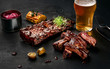 Pork ribs in barbecue sauce and a glass of beer on a black slate dish. A great snack to beer on a dark stone background. Top view with copy space