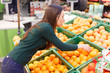 © vladdeep - A young woman in a store chooses oranges.