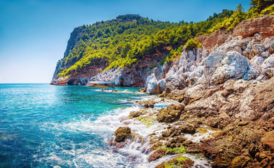 Wall Mural - Scenic seascape of sea with stones and rocks on beach and mountains with green forest on peak. Tropical summer nature landscape of Turkey on sunny summer day. Hiking and travel adventure outdoors