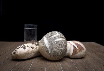 Wall Mural - Artisan breads and water glasses on wooden table in dark room