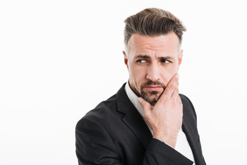 Canvas Print - Photo of attractive businessman in suit looking aside with brooding look and touching his chin, isolated over white background