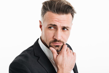 Sticker - Photo of attractive brunette businessman in formal wear looking aside with brooding look and touching his chin, isolated over white background