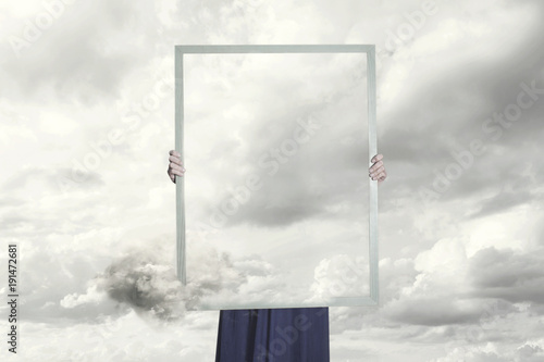 Fototapeta surreal moment of a woman hiding behind a picture of clouds equal to the landsca