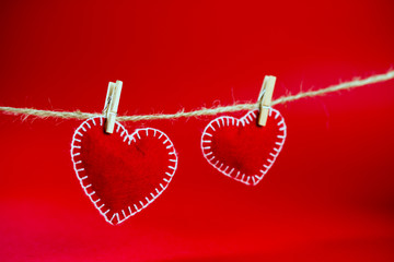 two decorative hearts made of red fumirana sewn with a white thread, clothespins on a rope, on a red background. Happy Valentine's Day symbol. selective focus. close-up. can be used as a background