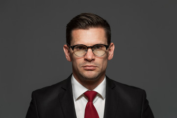 Wall Mural - An angry businessman in formal suit and glasses looks at the camera on gray background