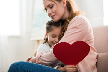 Wall Mural - happy mother and daughter with red heart symbol hugging at home