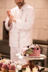 Wall Mural - selective focus of cake, cupcakes and confectioner in restaurant kitchen