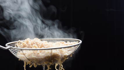 Noodles in a basket that just boiled from hot soup pot with steam selective focus,soft focus