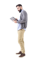 Wall Mural - Professional young adult businessman using and looking at tablet computer. Side view. Full body length portrait isolated on white studio background. 