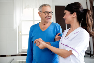 Young beautiful nurse helps to senior man at bathroom