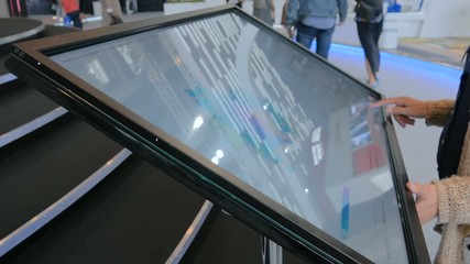 Woman using interactive touchscreen display at urban exhibition - scrolling and touching. Education and technology concept