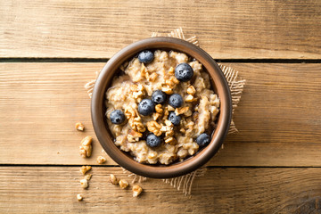 Wall Mural - Oatmeal porridge with blueberries, walnuts and honey in ceramic bowl on wooden background.