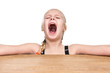 Little girl sitting at table with hands to side and screaming isolated on white background