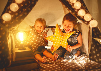 Wall Mural - happy family children brother and sister play, laugh and hug   in dark tent in playroom