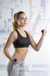 © SKfoto - Beautiful fitness girl in black top with purple dumbbells on the background of fitness room.