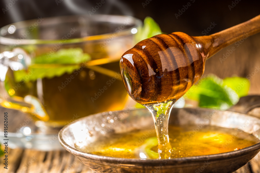 Honey. Honey and honey dipper on rustic oak table. Hot herb tea in the background - obrazy, fototapety, plakaty 