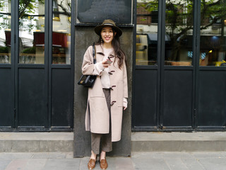 Beautiful young brunette woman wearing a beige coat in autumn city. Outdoor fashion portrait of glamour young Chinese cheerful stylish lady in street. Emotions, people, beauty and lifestyle concept.