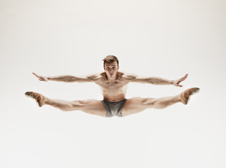 Athletic ballet dancer in a perfect shape performing over the grey background.