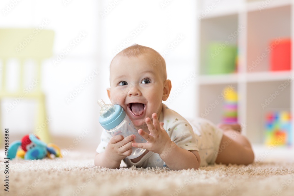 Cute baby boy drinking from bottle. Smiling child is 7 months old. - obrazy, fototapety, plakaty 