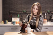 © Надежда Манахова - A beautiful young woman pours tea from a transparent teapot into a white mug in a loft kitchen, a dark interior. The girl is dressed in a striped blouse and a black corset. Modern design. life style.