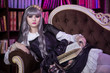 © Надежда Манахова - A beautiful woman in the shape of a lolita, a doll with cat ears sitting on a sofa in a library with a book in her hands and reading. Japanese street fashion. A doll in a dress. Copy space.