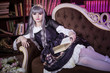 © Надежда Манахова - A beautiful woman in the shape of a lolita, a doll with cat ears sitting on a sofa in a library with a book in her hands and reading. Japanese street fashion. A doll in a dress. Copy space.