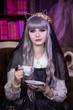 © Надежда Манахова - Beautiful woman in a doll dress, in a gray wig sits on a background of books with a cup of tea. Kawai Lolita. Japanese street fashion.
