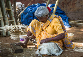 Indian elder lady on yellow saree sitting on the ground making bamboo baskets on the street in Mysore, Karnataka, India. Hard work, humble, poor old woman blue collar job concept