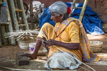 Indian elder lady on yellow saree sitting on the ground making bamboo baskets on the street in Mysore, Karnataka, India. Rural village hard worker woman