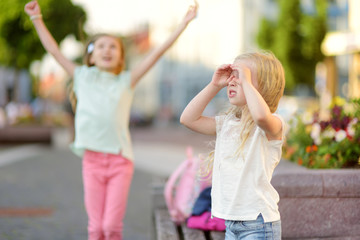 Two cute little sisters having a walk together in a city on warm and sunny summer day.