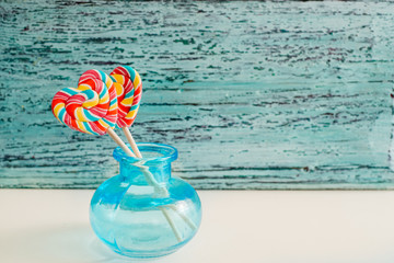 Two colored striped rainbow candy on a stick in the form of a heart. on a blue old vintage wooden background. The concept for Valentine's Day.