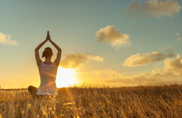 Woman meditating in a open filed at sunset. 