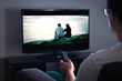 © terovesalainen - Man watching tv or streaming movie or series with smart tv at home. Film or show on television screen. Person holding the remote control or switching channel. Turning on or off tv.