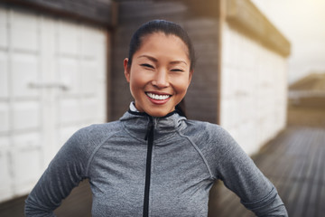 Smiling young Asian woman standing outside before a jog