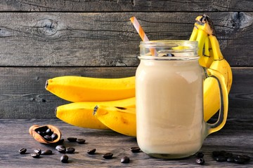 Wall Mural - coffee, banana smoothie in a mason jar with coffee beans and bananas in background. side view agains