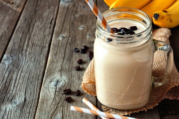 Wall Mural - coffee, banana smoothie in a mason jar. side view with copy space over a rustic wood background.
