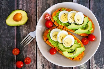 Wall Mural - Sweet potato toasts with avocado, eggs and chia seeds on a plate. Top view on a dark wood background.