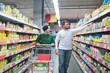 © bodnarphoto - A young beautiful couple walking with a supermarket cart and choosing products. Family shopping at a supermarket