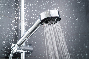 Fresh shower behind wet glass window with water drops splashing. Water running from shower head and faucet in modern bathroom.