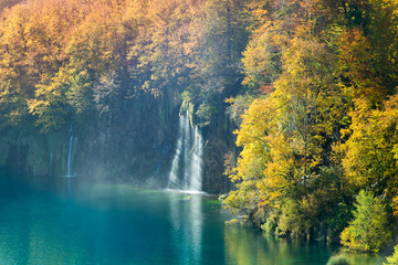  An amazing display of autumn in Plitvice Lakes National Park. The great variance of changing colors of the trees and two waterfalls falling into the turquoise colored lake water.