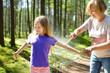© MNStudio - Middle age woman applying insect repellent to her granddaughter before forest hike beautiful summer day. Protecting children from biting insects at summer.