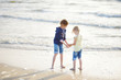 © MNStudio - Two little sisters having fun on a sandy beach on warm and sunny summer day. Kids playing by the ocean.