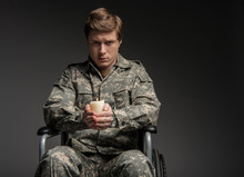 Unhappy Paralyzed Soldier Looking At Camera With Frustrated Look. He Is Sitting In Invalid Chair And Holding Suppository. Isolated On Grey Background. Copy Space In Right Side