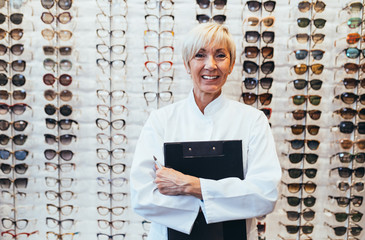 Poster - Senior female ophthalmologist standing in optical store. 