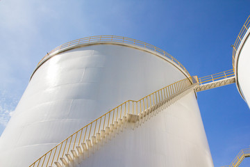 white storage tanks, fuel steel silos with yellow stair ladder against blue sky